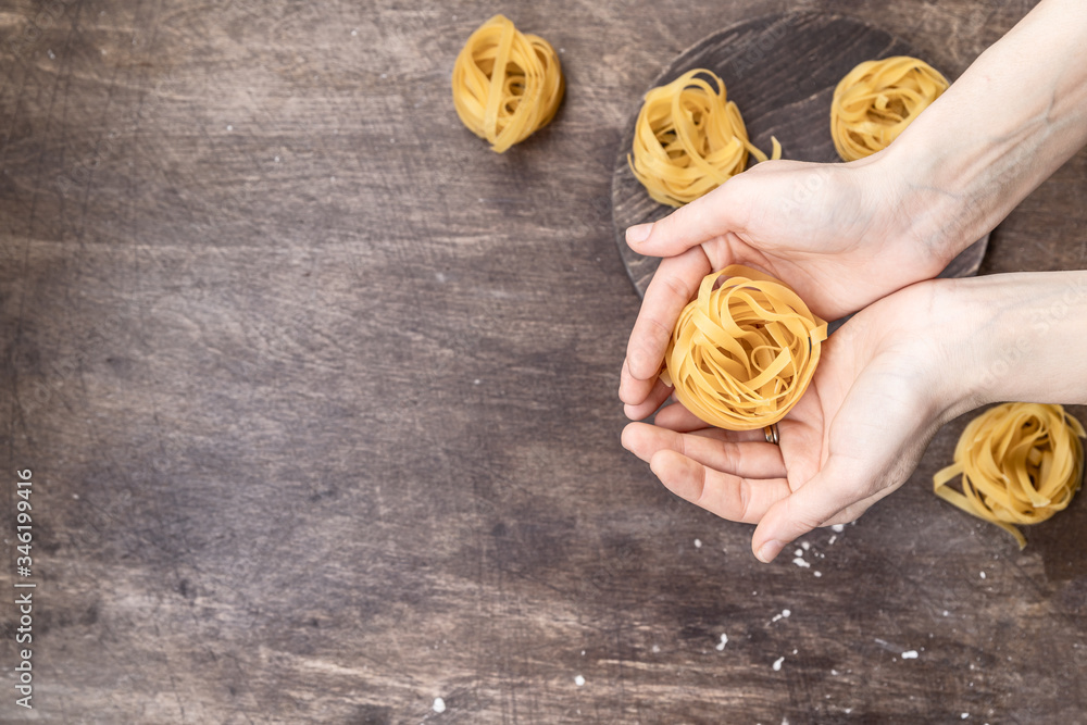 Italian nest paste in female hands on a dark brown plywood table. Mediterranean cuisine cover Italian nest paste in female hands on a dark brown plywood table. Mediterranean cuisine cover