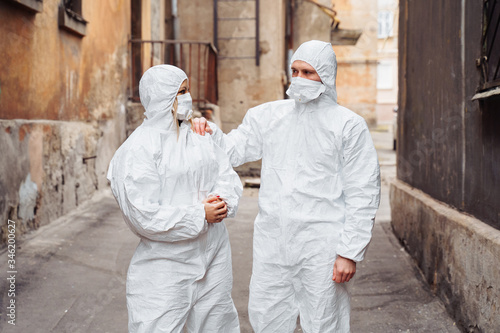Doctors in protective suits and protective masks stand on the street with serious faces. Walking along the street, guy leads woman foward - they are very determined. The concept of coronirus covid-19