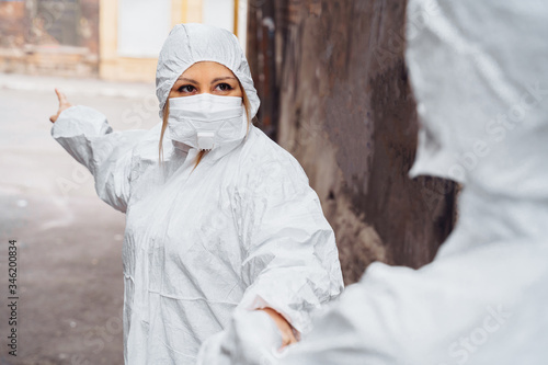 Woman medic in a protective suit and medical mask pulling doctor to save lives. They are scared, but ready to help people. Woman showing the direction where to go. Coronavirus concept. Covid-19