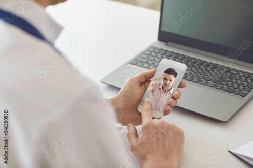 Male doctor online. Doctor speaks with a patient using a phone sitting behind a straw in a clinic office. Online medical consultation.