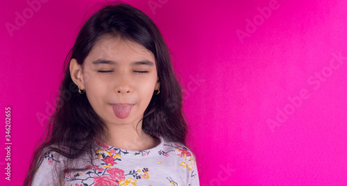 Little funny girl with a collorful mask. Excitement and fascination concept. Close up portrait. Coronavirus pink background. foolish grimaces comical crazy gesture. Funny expression. Covid-19. 