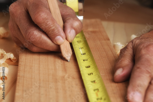 Closeup of a carpenter measuring an marking a board for cutting. Man is unrecognizable, hands only.