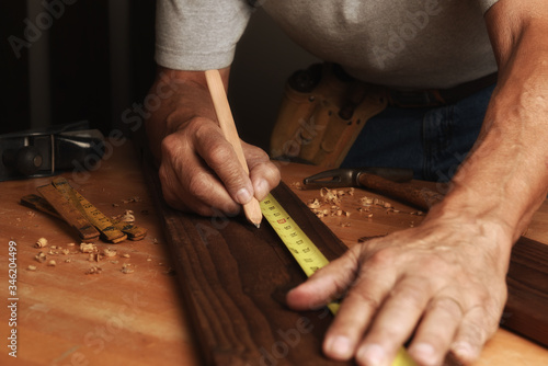 Closeup of a man in his workshop marking a board for cutting.