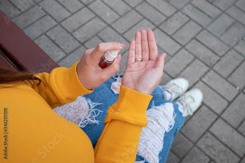 A young girl in a yellow sweater disinfects the hands with a spray sanitizer
