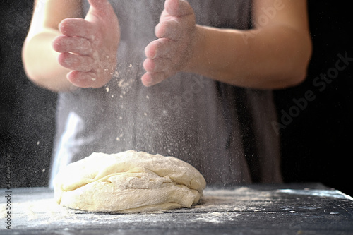 Making dough by hands at bakery or at home. Flour cloud in the air. Close up of woman chef hands preparing for kneading the dough on the table, powdering with flour. dough for bread, pasta or pizza