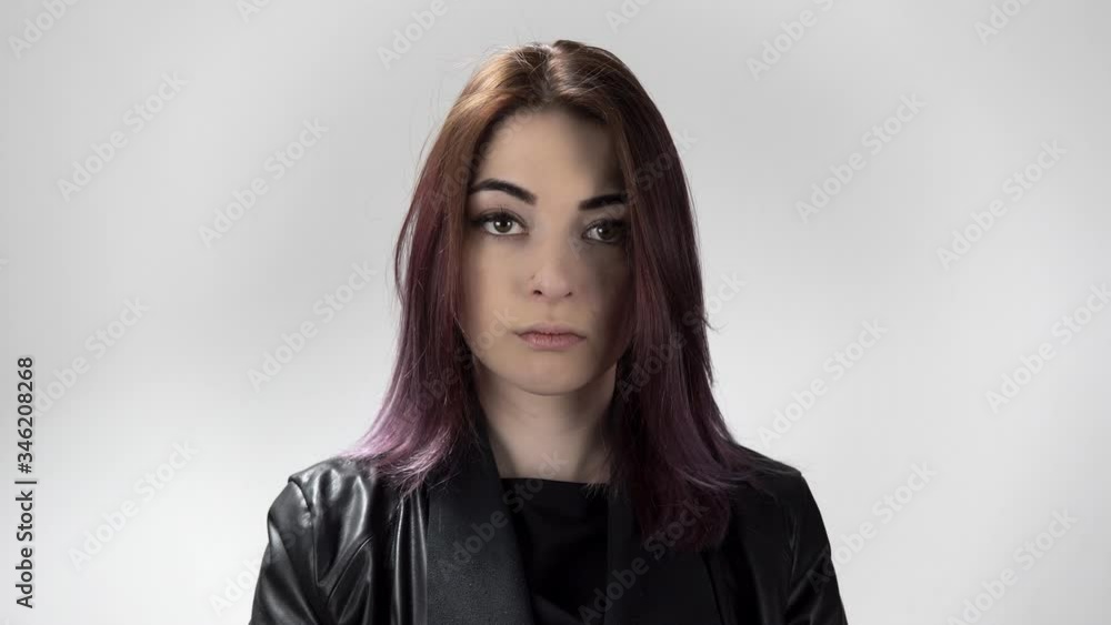 Portrait of young woman with coloured hair sadly watching in camera and down. Girl in black leather jacket standing in the studio with white background. Theme of showing different facial expressions. Portrait of young woman with coloured hair sadly watching in camera and down. Girl in black leather jacket standing in the studio with white background. Theme of showing different facial expressions.