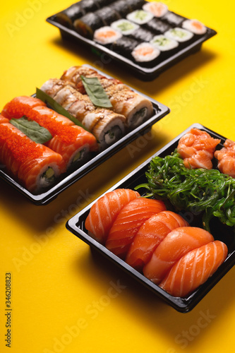 Sushi with fresh fish salmon and eel delivery in containers to the house on a bright yellow background.