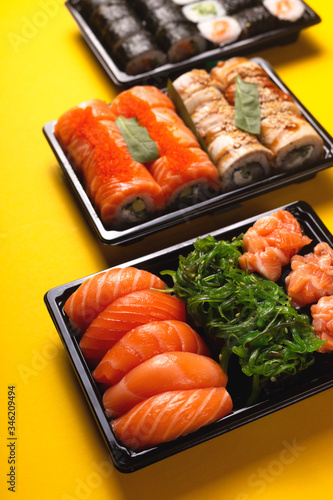 Sushi with fresh fish salmon and eel delivery in containers to the house on a bright yellow background.