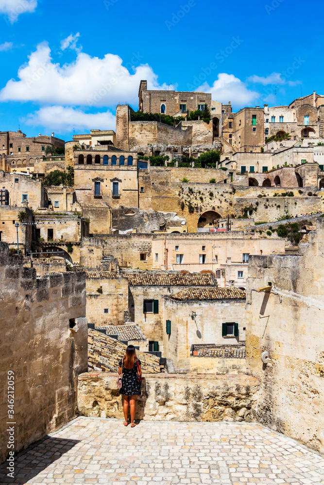 Old town sunny summer view of Matera, Province of Matera, Basilicata Region, Italy with a rear view of an unidentified young female tourist