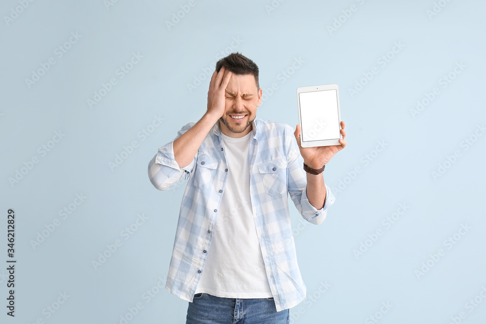 Troubled man with tablet computer on color background
