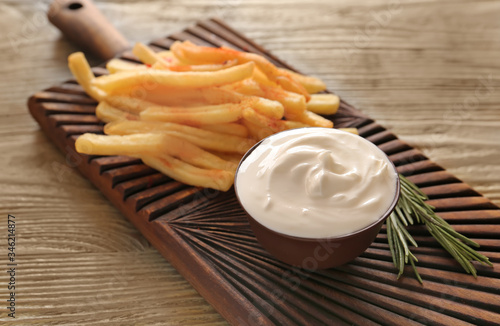 Board with tasty sour cream and french fries on table