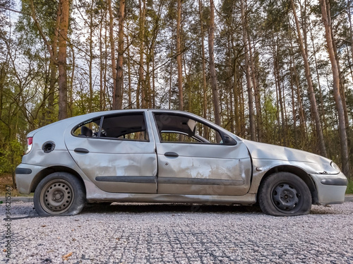 Low angle side view of dumped and damaged car wreck at a car park in a forest.
