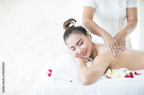 Asian woman massaging spa with salt. Beauty therapist pouring salt scrub on woman back at health spa.