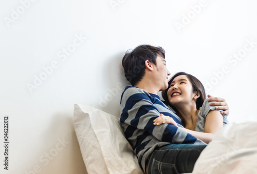 Happy & smiling attractive young cute Asian couple in love hugging and holding hands on bed in bedroom at home together. Happiness family of beautiful romantic married lover or marriage relationship