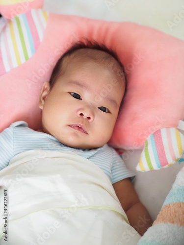 A cute Asian 2-month-old baby girl is lying down on a soft and comfortable mattress, with pillow and blanket. Close up shot.