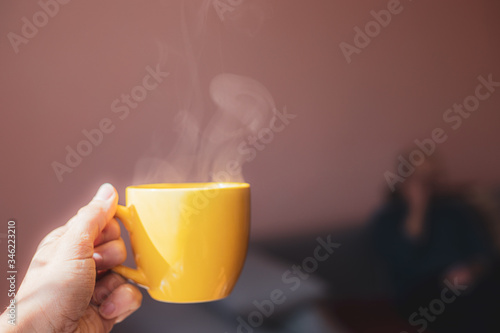 Yellow cup with hot streaming tea drink in hand