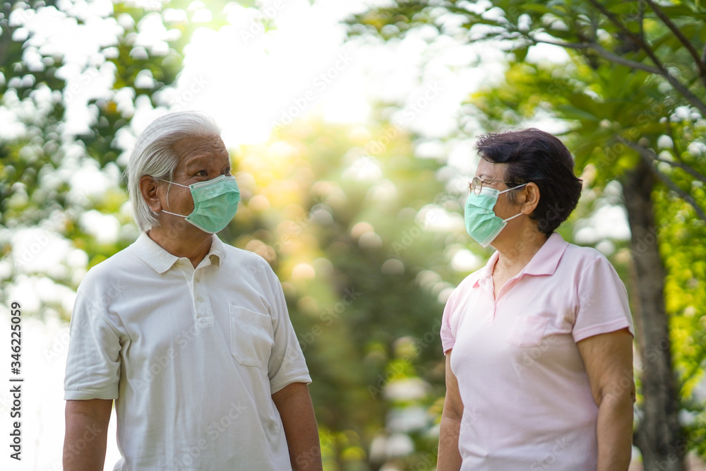 Asian elderly couple wearing surgical mask while walking in the park and keep social distancing during 
covid-19 outbreak