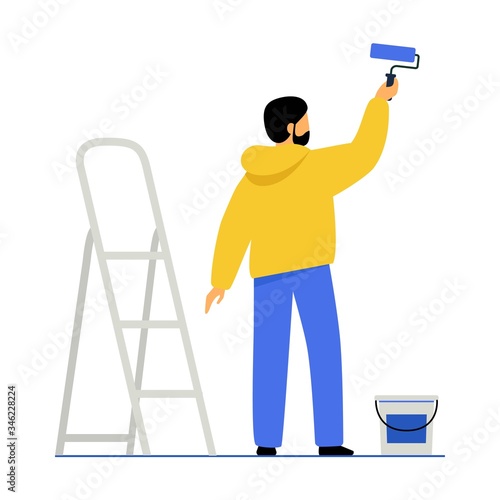 A man paints a wall with paint. The guy holds a paint roller in his hand, next to it is a stepladder and a can of paint.