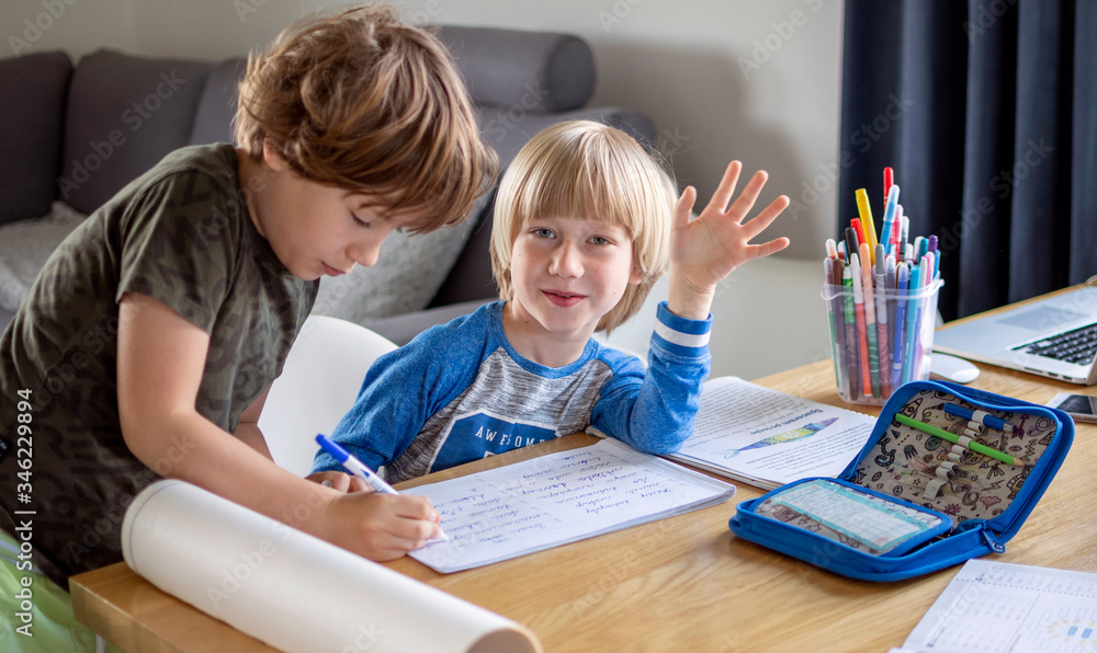 Two boys doing their homework, studying at home in living room. Older brother helps the younger one. Two boys doing their homework, studying at home in living room. Older brother helps the younger one.