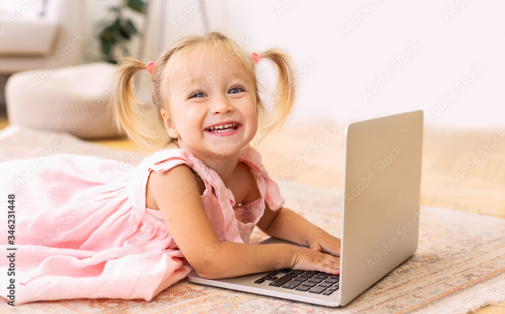 Adorable little girl using laptop lying on floor