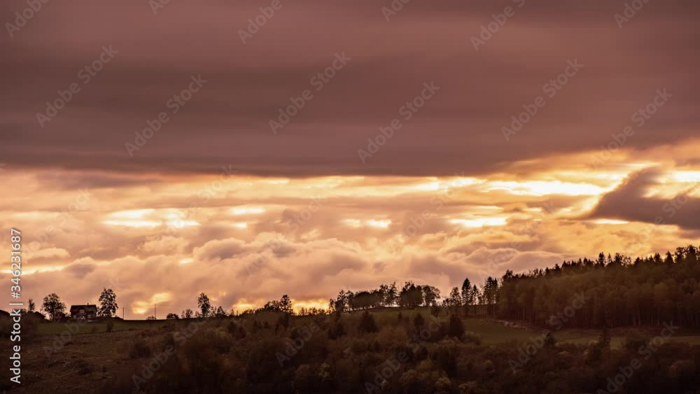 Magnificent sunset in Norway. The sky is burning with orange and yellow, clouds whirling, twisting, and turning. Dark silhouettes of the trees and houses seen on the horizon. Magnificent sunset in Norway. The sky is burning with orange and yellow, clouds whirling, twisting, and turning. Dark silhouettes of the trees and houses seen on the horizon.