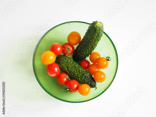 Red and yellow cherry tomatoes and two cucumbers in a transparent green bowl