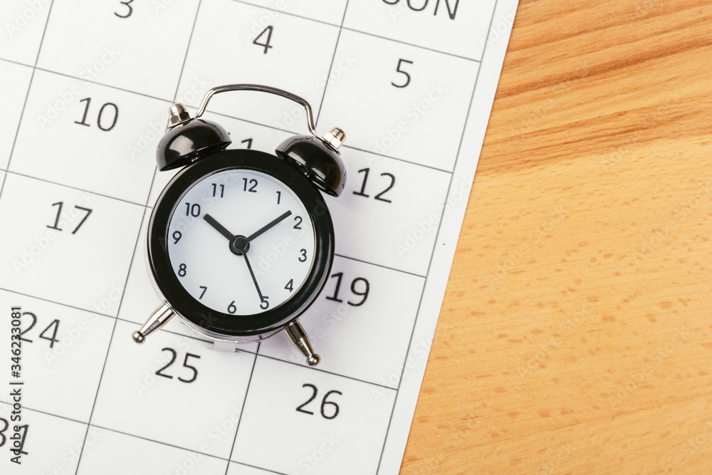 Flat lay or top view of black alarm clock with white calendar on wooden board with copy space, schedule for vacation, reminder for business appointment Flat lay or top view of black alarm clock with white calendar on wooden board with copy space, schedule for vacation, reminder for business appointment