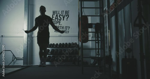 Male cross-fit athlete performs double unders with skipping jump rope inside a dark gym photo