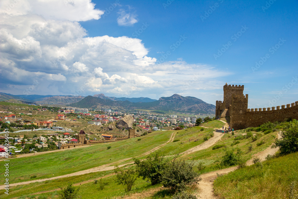 The view to ancient fortress and the town at foot of the mountains in sunny day. Genoese fortress, Sudak, Crimea. Historic old building. Monument of architecture.