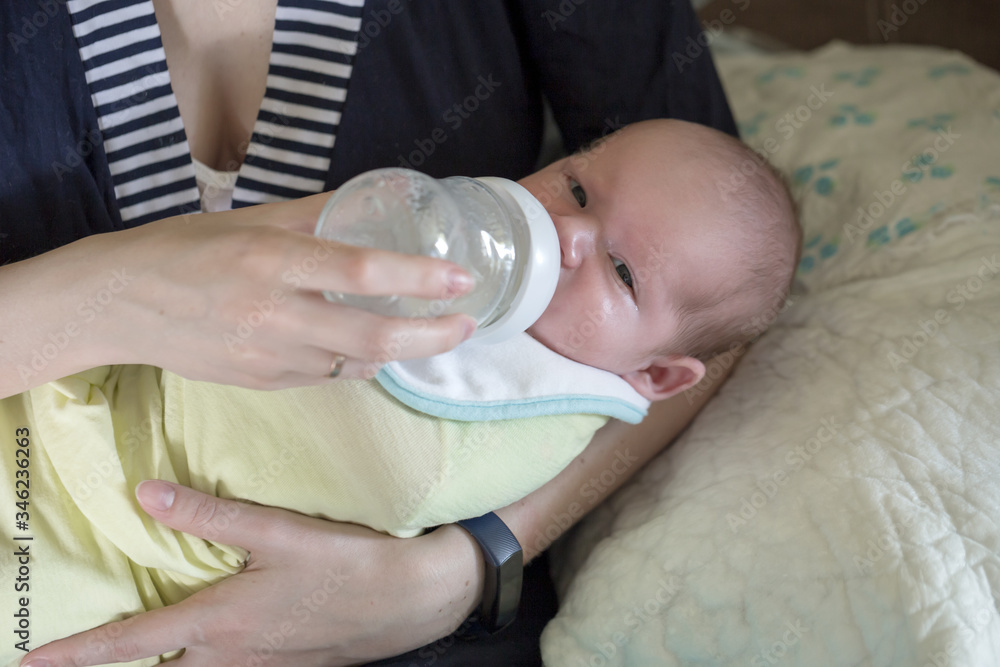 Little infant baby lying on mothers hand drinking milk from bottle. Baby food. Mom and child.