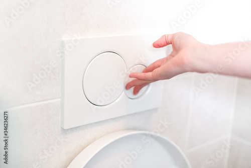 Woman hand flushing toilet button - press the water button, flush the toilet, health concept photo
