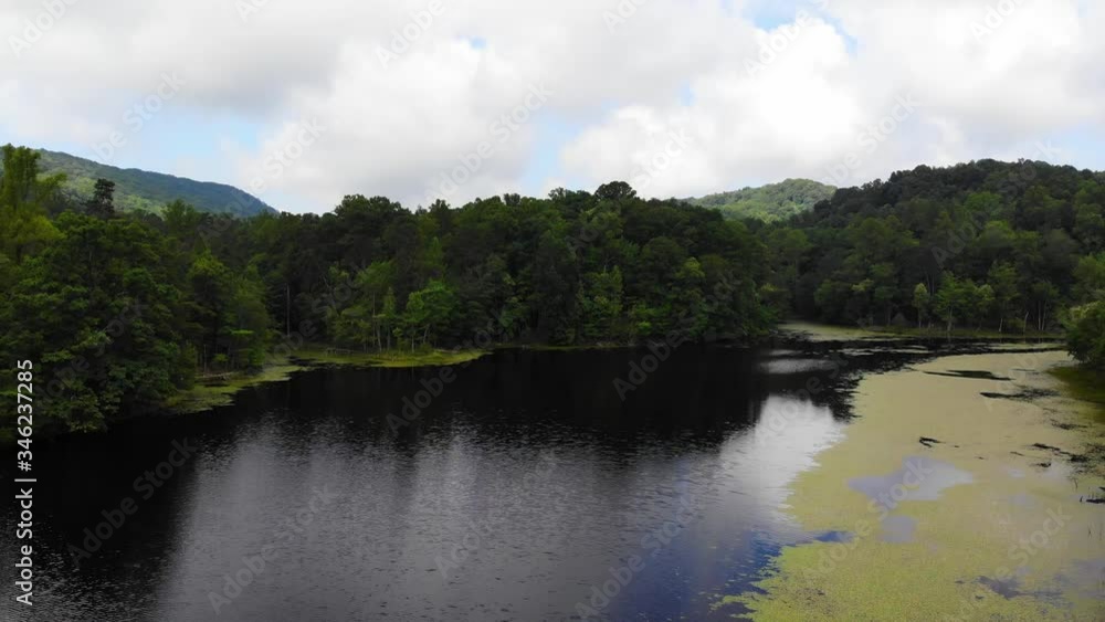 Flying towards several small channels of water, rising above the trees to reveal rolling hills of mountain that surrounds the lake. Sun illuminating portions of the valleys and hills. Flying towards several small channels of water, rising above the trees to reveal rolling hills of mountain that surrounds the lake. Sun illuminating portions of the valleys and hills.