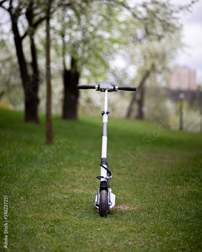 white electric scooter on a green lawn in summer. The concept of two-wheeled urban environmental transport.