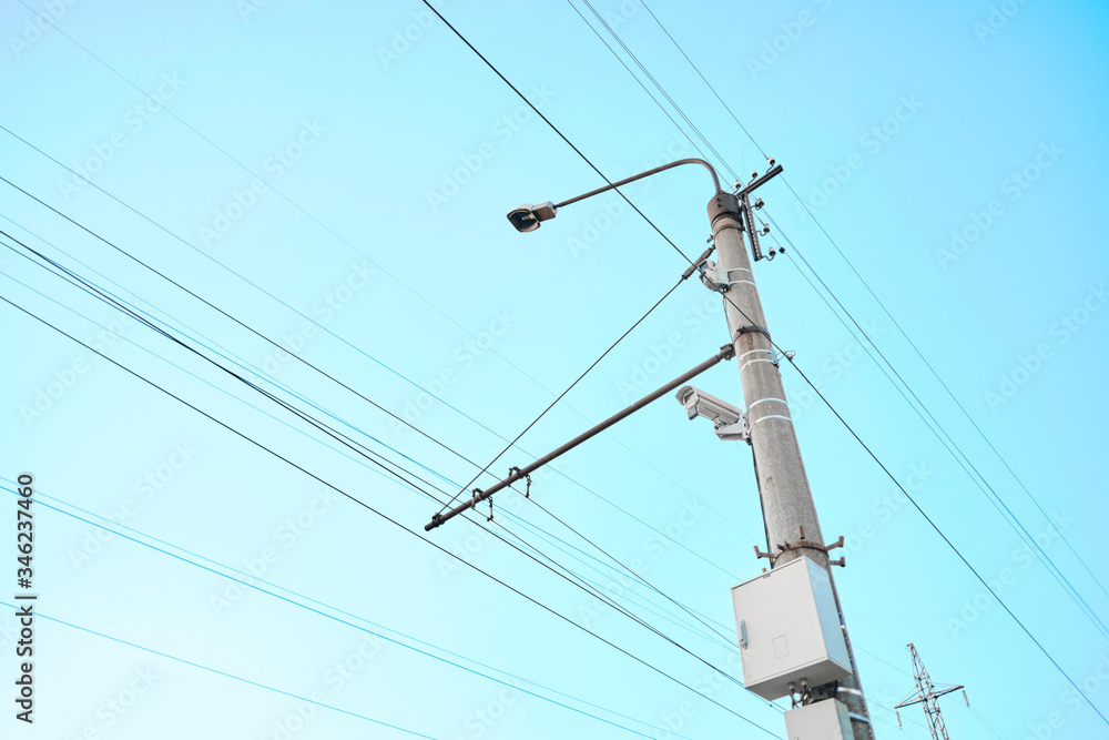 Outdoor surveillance camera on pole with cables. Against a bright blue sky background. Outdoor surveillance camera on pole with cables. Against a bright blue sky background.