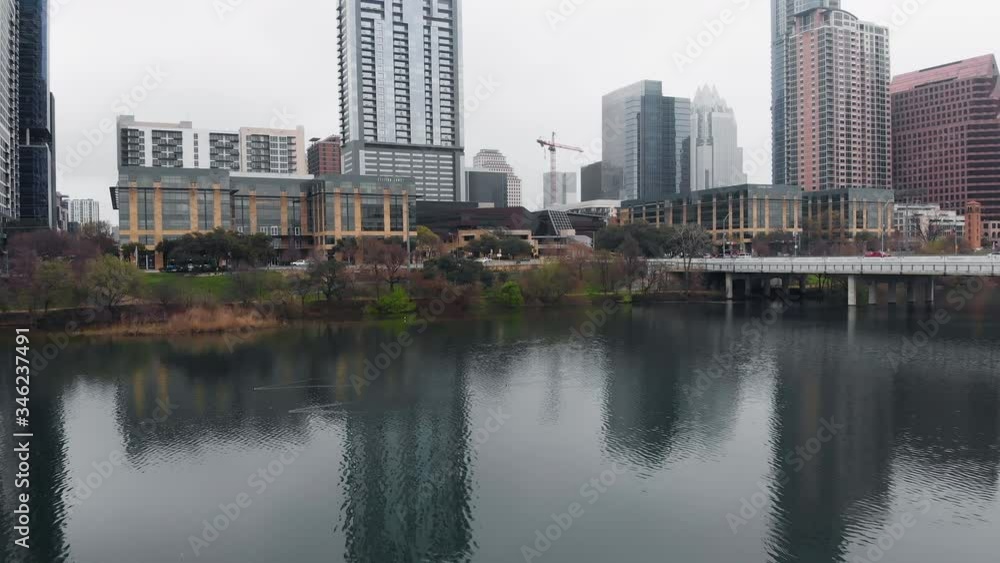A drone flies in reverse above the Colorado River and Ladybird Lake, revealing the Austin, Texas skyline on a cloudy morning. A drone flies in reverse above the Colorado River and Ladybird Lake, revealing the Austin, Texas skyline on a cloudy morning.