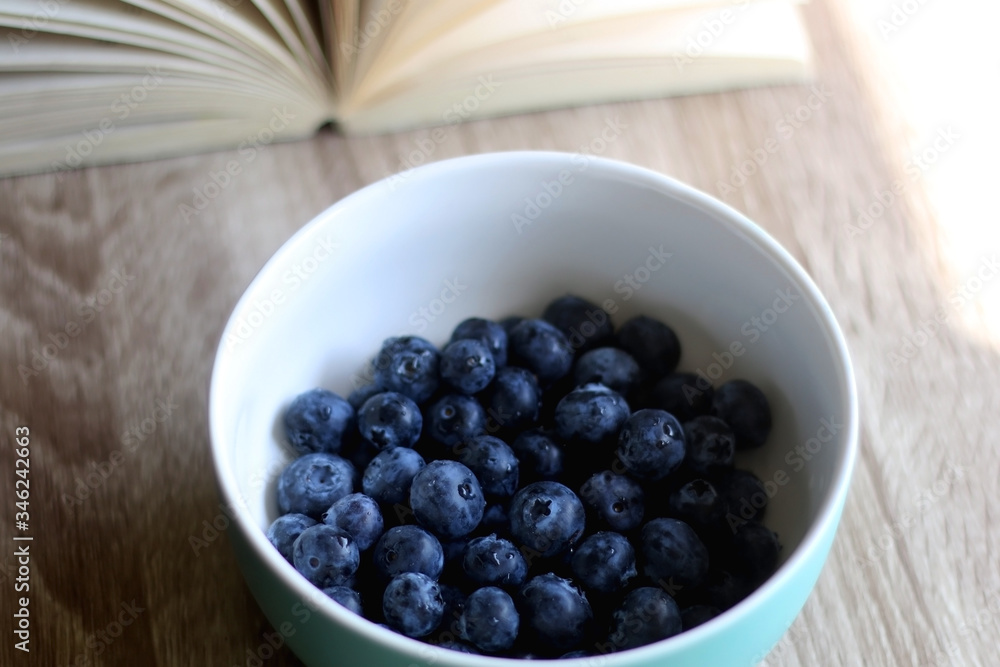 Bowl of fresh blueberries and open book on a table. Selective focus. Bowl of fresh blueberries and open book on a table. Selective focus.