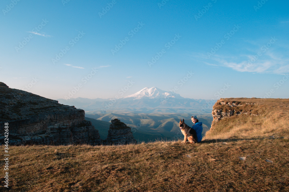 Girl and dog on the background of Elbrus. A girl and a German shepherd travel through the mountains together.