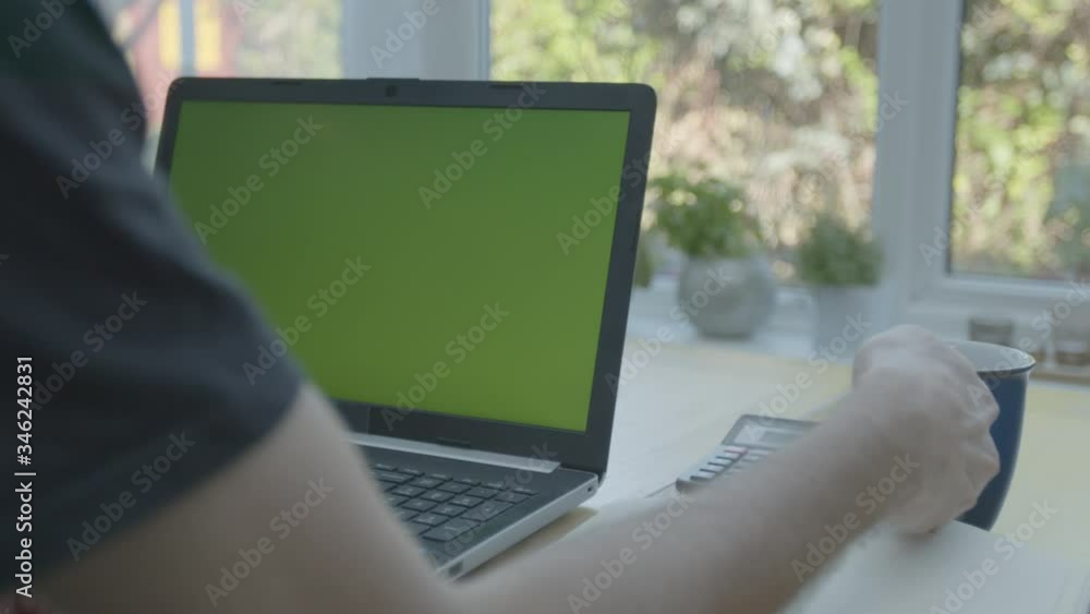 Working from home in the conservatory typing on green screen laptop taking a sip of coffee Working from home in the conservatory typing on green screen laptop taking a sip of coffee