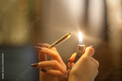 Young woman with pretty manicured nails is holding a lighter and about to spark and light a legal pre rolled marijuana bud joint in organic hemp rolling papers for THC smoking