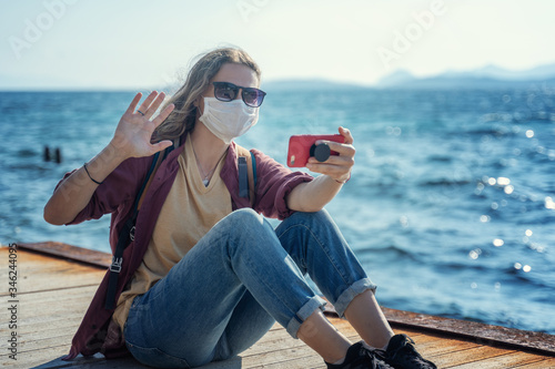 Foto One young girl a woman in a mask and sunglasses sits on a wooden pier on the seashore with a smartphone in her hands