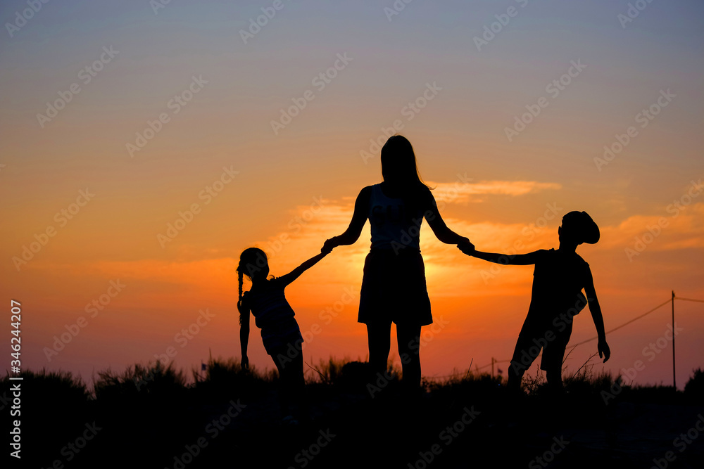 Mother and children hold hands in the background of the sunset.