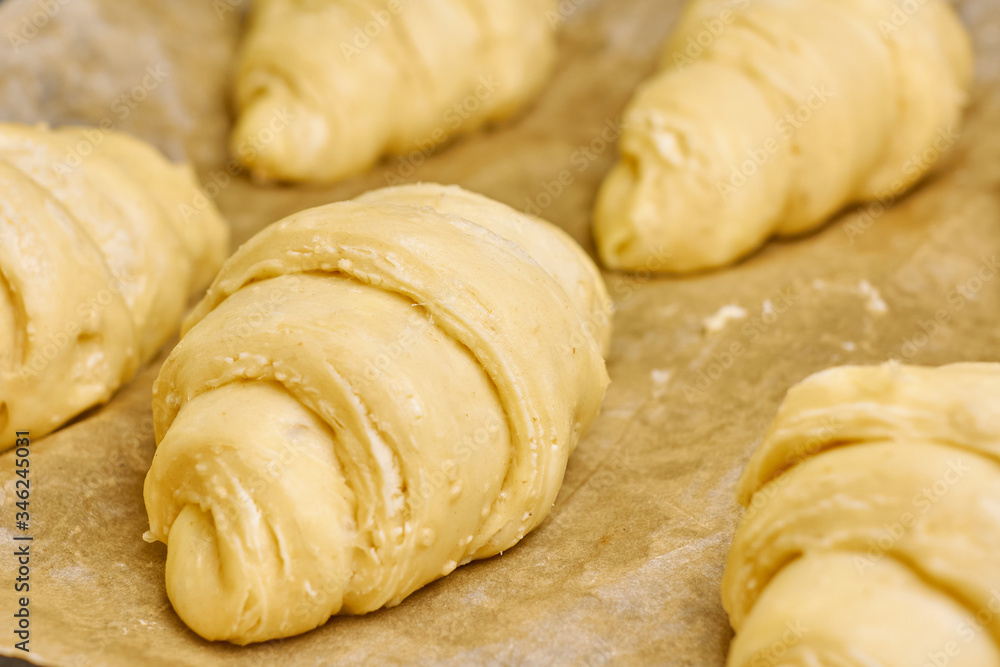 Producing of classic croissants from rolled layered dough. at home. Raw classic crescent rolls on a baking paper. Traditional french pastry