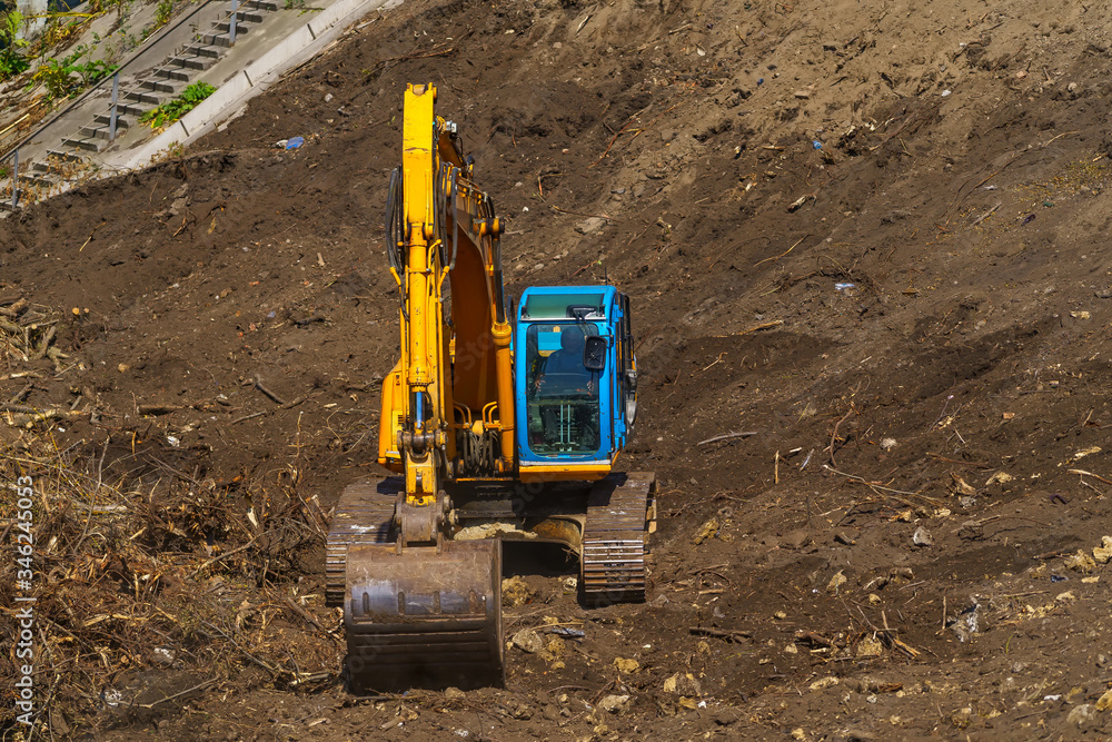 Yellow backhoe with hydraulic piston arm against clear blue sky. Heavy machine for excavation in construction site. Hydraulic machinery. Huge bulldozer. Heavy machine industry. Mechanical engineering. Yellow backhoe with hydraulic piston arm against clear blue sky. Heavy machine for excavation in construction site. Hydraulic machinery. Huge bulldozer. Heavy machine industry. Mechanical engineering.
