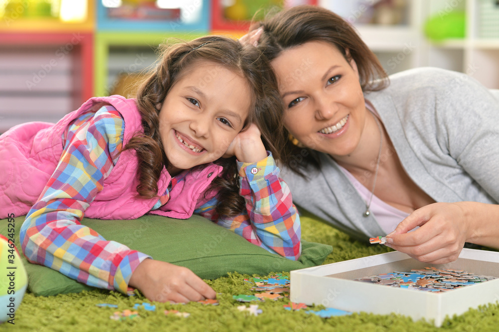 Fototapeta premium Close up portrait of mother with little daughter collecting puzzle