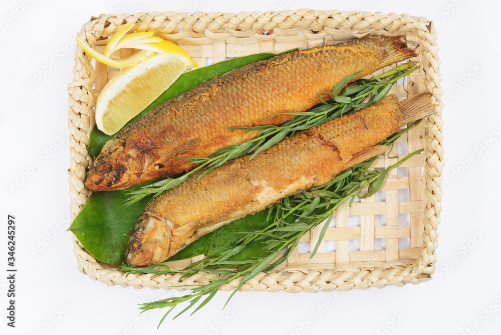 Grilled fish in a wicker basket with greens on a white background. Grilled fish in a wicker basket with greens on a white background.