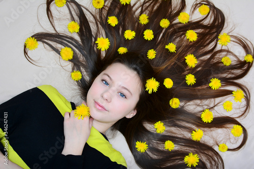 Portrait of a young girl with yellow dandelion flowers in her loose hair. View from above.