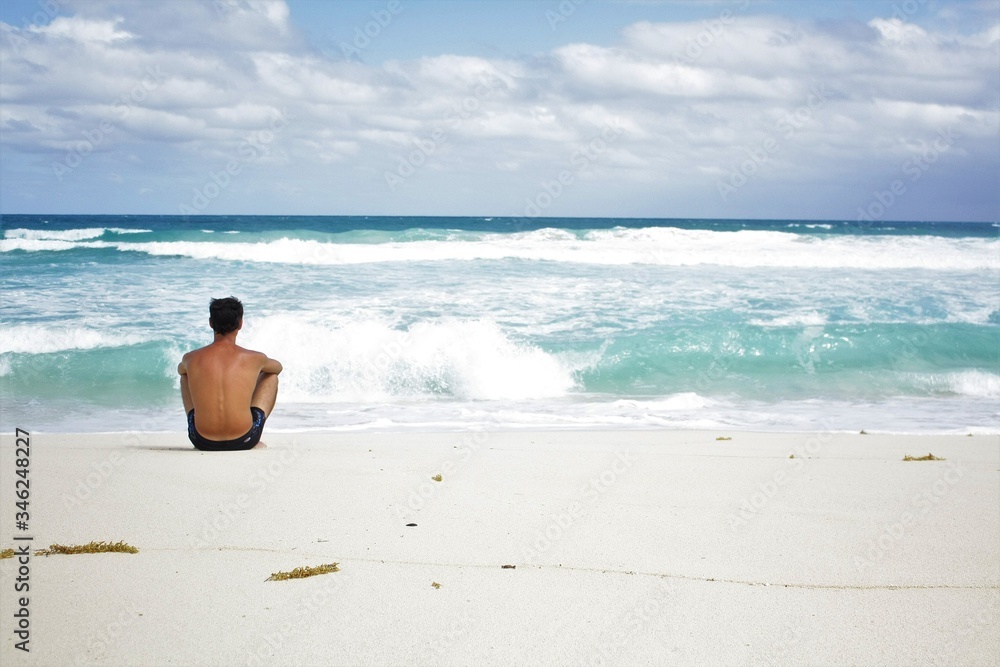 A man sits on a wild ocean beach