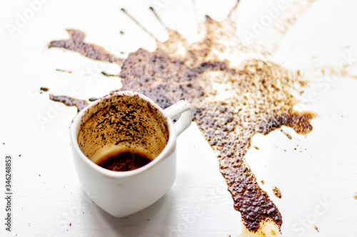 A Cup of custard coffee spilled on a white table background, side view. A beautiful spot from the coffee brew. Fortune-telling on coffee grounds. Layout for grunge advertising design, copy space.
