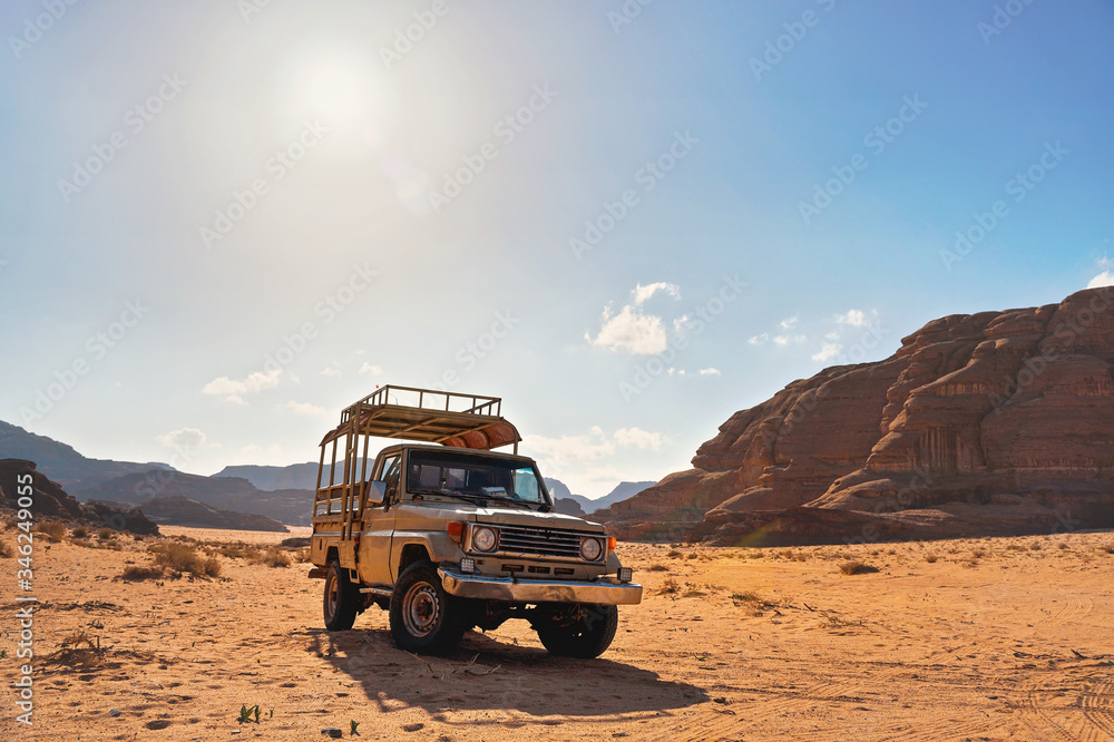 4WD off road vehicle parked in desert, backlight sun shines on mountains background - typical scenery of Wadi Rum, Jordan