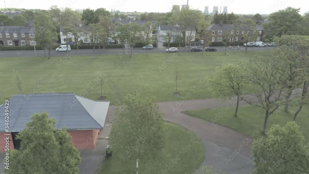 Aerial drone view across park green field to British town houses above trees Aerial drone view across park green field to British town houses above trees